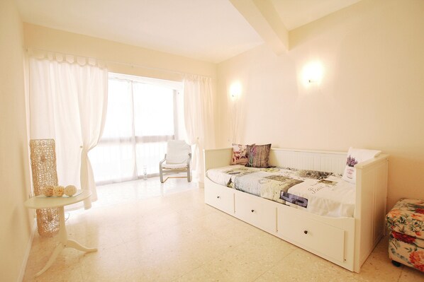 A bedroom with a bed, a chair, a small table, and a window with curtains.
