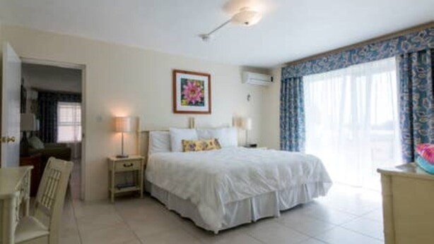 A hotel room with a large bed, a bedside table, a chair, a desk, and a window with curtains. - Clairfont, Jobson's Cove / Warwick Long Bay/ Horseshoe Beach -  APARTMENT 3 (Warwick)