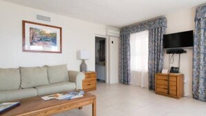 A living room with a sofa, a coffee table, a TV, and a patterned curtain. - Clairfont, Jobson's Cove / Warwick Long Bay/ Horseshoe Beach -  APARTMENT 3 (Warwick)
