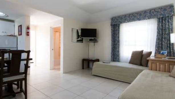 A room with a bed, a desk, a chair, a television, and a window with curtains. - Clairfont, Jobson's Cove / Warwick Long Bay/ Horseshoe Beach -  APARTMENT 5 (Warwick)