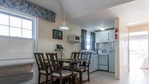 A dining area with a table and chairs, a microwave, and a refrigerator in the background. - Clairfont, Jobson's Cove / Warwick Long Bay/ Horseshoe Beach -  APARTMENT 5 (Warwick)