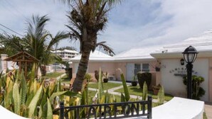 A hotel with a white facade, palm trees, and a well-maintained garden. - Clairfont, Jobson's Cove / Warwick Long Bay/ Horseshoe Beach -  APARTMENT 5 (Warwick)