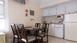 A compact kitchen with white cabinets, a microwave, and a refrigerator. There is a dining table with chairs and a fire extinguisher mounted on the wall. - Clairfont, Jobson's Cove / Warwick Long Bay/ Horseshoe Beach -  APARTMENT 6 (Warwick)
