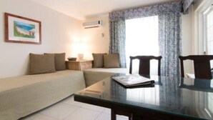 A living room with a sofa, a glass table, and a chair. There is a painting on the wall and a window with curtains. - Clairfont, Jobson's Cove / Warwick Long Bay/ Horseshoe Beach -  APARTMENT 6 (Warwick)