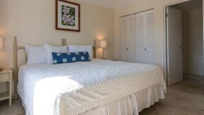 A bedroom with a bed, a nightstand, a bedside lamp, a framed picture on the wall, and a closet. - Clairfont, Jobson's Cove / Warwick Long Bay/ Horseshoe Beach -  APARTMENT 8 (Warwick)
