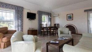 A living room with a sofa set, a coffee table, a dining table with chairs, a flat-screen TV mounted on the wall, and a fireplace. - Clairfont, Jobson's Cove / Warwick Long Bay/ Horseshoe Beach -  APARTMENT 8 (Warwick)