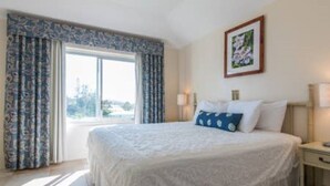 A hotel room with a large bed, two bedside tables, a window with curtains, and a framed picture on the wall. - Clairfont, Jobson's Cove / Warwick Long Bay/ Horseshoe Beach -  APARTMENT 8 (Warwick)
