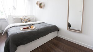A modern bedroom with a bed, a bedside table, a tray with breakfast, and a large mirror.