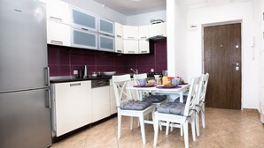 A modern kitchen with white cabinets, a built-in oven, and a dining area with white chairs and a purple table.