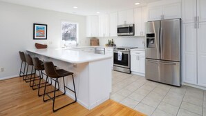 Una cocina moderna con armarios blancos, electrodomésticos de acero inoxidable y una isla central con taburetes de bar.