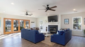Amplia sala de estar con dos sofás azules, una chimenea, ventiladores de techo y ventanas grandes.