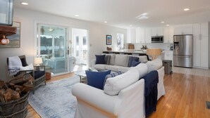 Un espacio habitable amplio con un sofá blanco, una mesa de comedor y una cocina con armarios blancos y electrodomésticos de acero inoxidable.