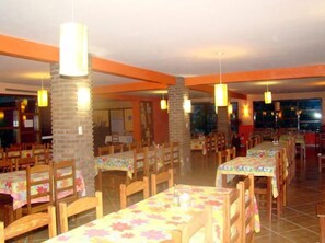 Un restaurant doté de nombreuses tables et chaises, de piliers en briques et de luminaires suspendus.