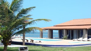 A pool area with lounge chairs, a sign for 'SALAO DE CAFÉ', and a building with a tiled roof.