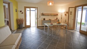 Una sala de estar moderna con un sofá, una mesa de comedor con sillas, una zona de cocina con mostrador y estanterías, y un ventanal con vistas.