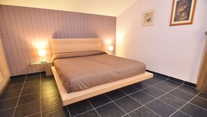 Un dormitorio con una cama, dos mesitas de noche, un tablero auxiliar y dos cuadros enmarcados.