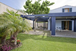 A covered patio area with a pergola, a palm tree, and a garden with purple flowers. - Luxury Villa (Ragusa)