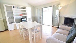 Un salon avec une table à manger blanche, des chaises, un canapé gris et une cheminée.
