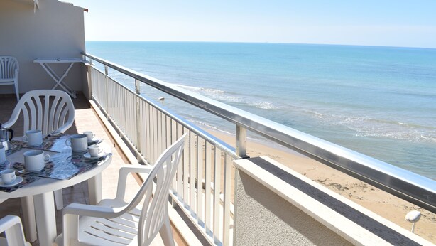 Un balcon avec une table dressée pour deux personnes, donnant sur une plage.