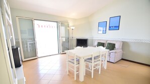Une pièce avec une table et des chaises blanches, un canapé, une cheminée et une porte-fenêtre coulissante donnant sur un espace extérieur.