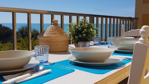 A dining table set with bowls, glasses, and cutlery on a balcony with a view of the sea. - Sitting on the beach (Santa Croce Camerina)