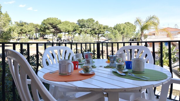 A white table with chairs on a balcony, set with tea cups and saucers, overlooking a tree-lined area. - Center Beach (Ragusa)