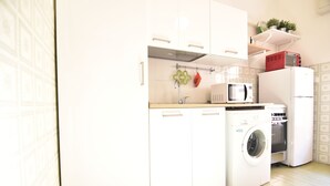 A compact kitchen with white cabinets, a washing machine, a microwave, and a refrigerator. - Center Beach (Ragusa)