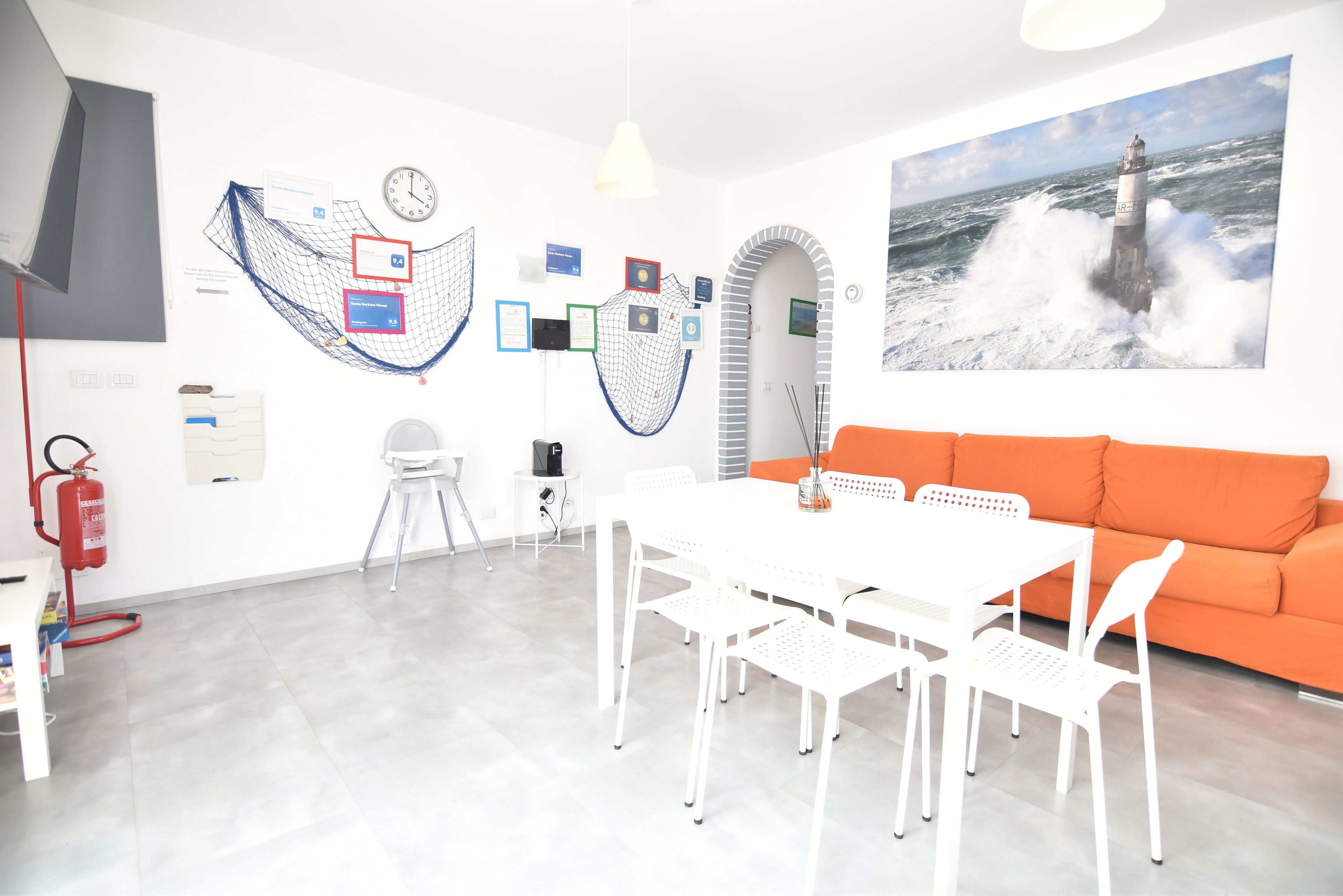 Une pièce moderne avec une table blanche, un canapé orange et un tableau représentant un phare.