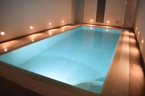 A rectangular indoor swimming pool with a smooth, reflective surface, surrounded by walls with recessed lighting. - Santa Barbara House (Ragusa)