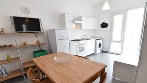 Una cocina moderna con armarios blancos, horno empotrado y un lavamanos. Hay una mesa de comedor con sillas y un televisor montado en un estante.