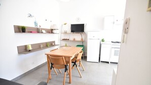 Una cocina moderna con una mesa y sillas de madera, televisión integrada y muebles de cocina blancos.