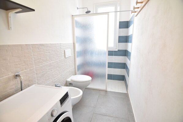 A compact bathroom with a washing machine, toilet, and shower area. - Casa del mar (Ragusa)