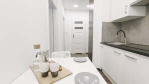 Une cuisine moderne avec des armoires blanches, un comptoir noir et un évier en acier inoxydable. On y trouve deux assiettes blanches et une planche à découper en bois, sur laquelle sont posées des tasses et un bocal.
