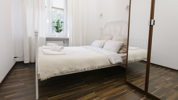 Une chambre à coucher au style minimaliste, avec un lit, une fenêtre avec des rideaux, une plante en pot et un miroir.