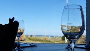 Una mesa con dos copas de vino y un plato, con vista al mar y un paisaje con césped.