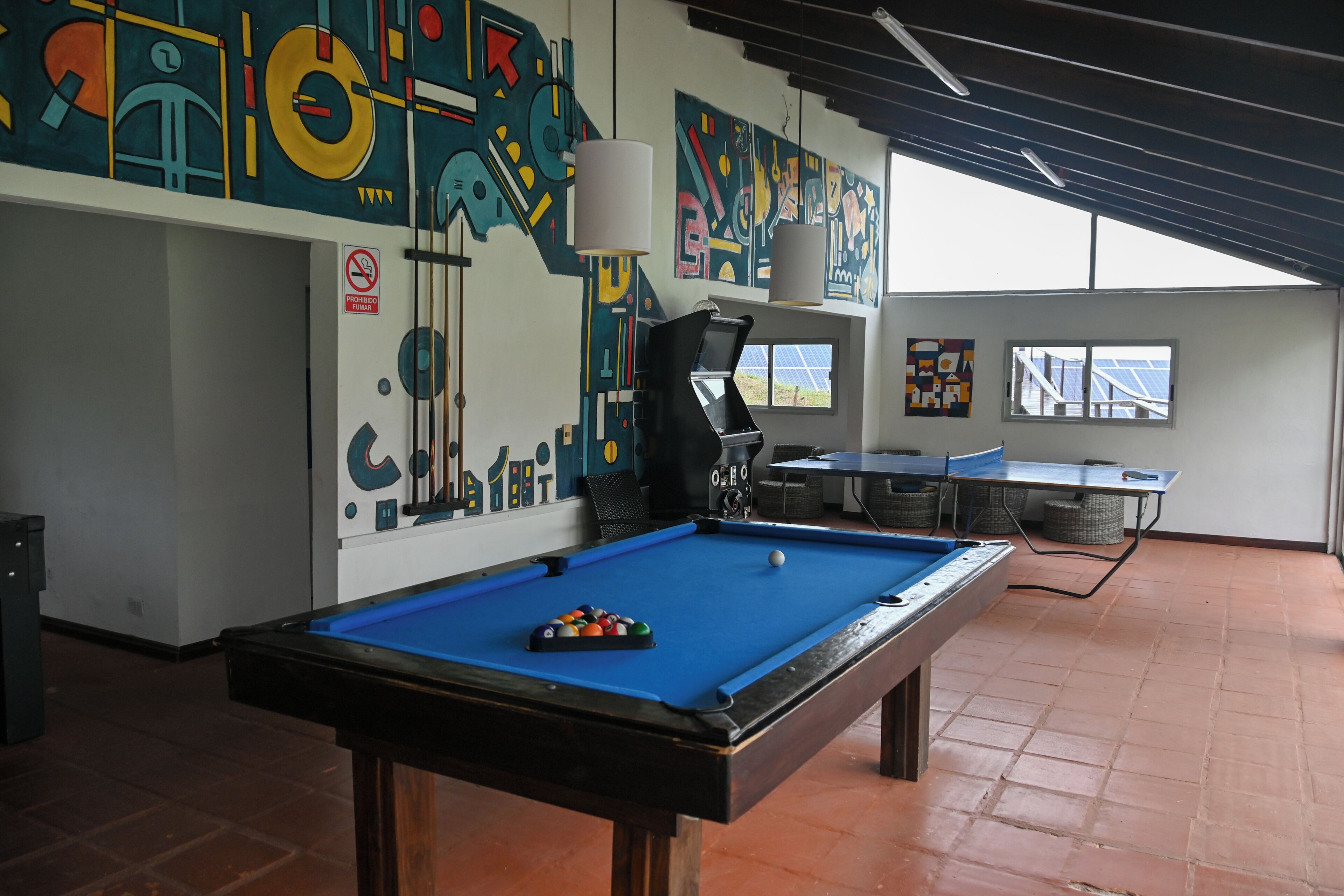 A pool table with balls, a billiards table, and abstract wall art in a room with a tiled floor and a window.