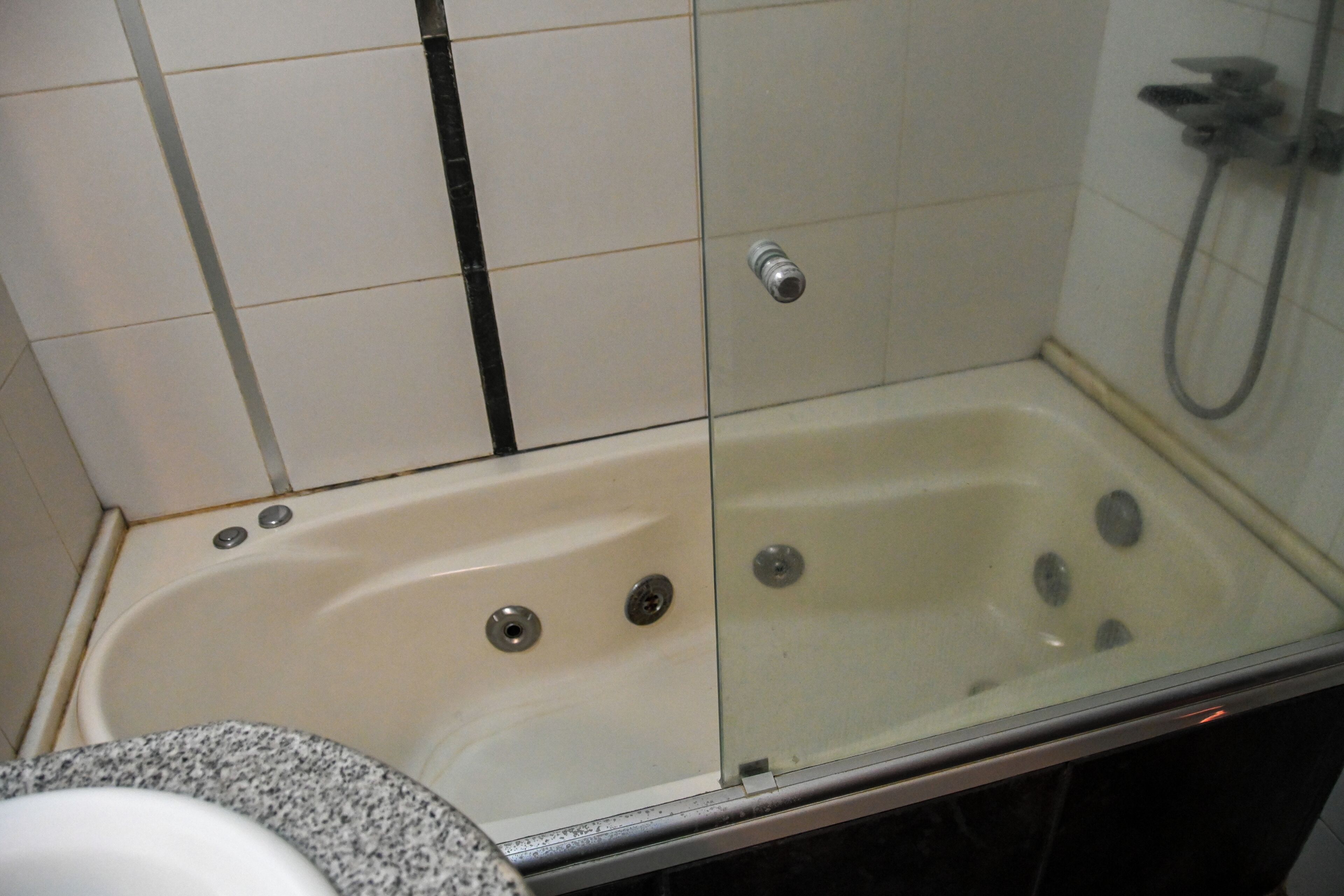 Un baño con bañera de hidromasaje con mampara de vidrio, ducha y retrete.
