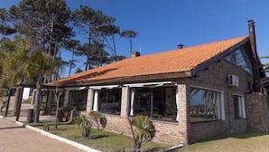 Un edificio de ladrillo con tejado de baldosas, ventanas grandes y un pequeño jardín con palmeras.