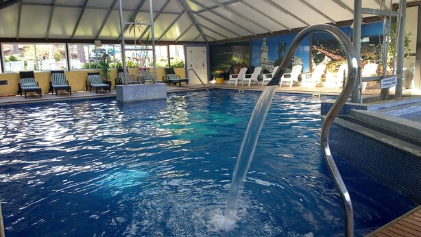 Una piscina interior con agua cristalina, una escalera metálica y sillones de descanso alrededor del borde.