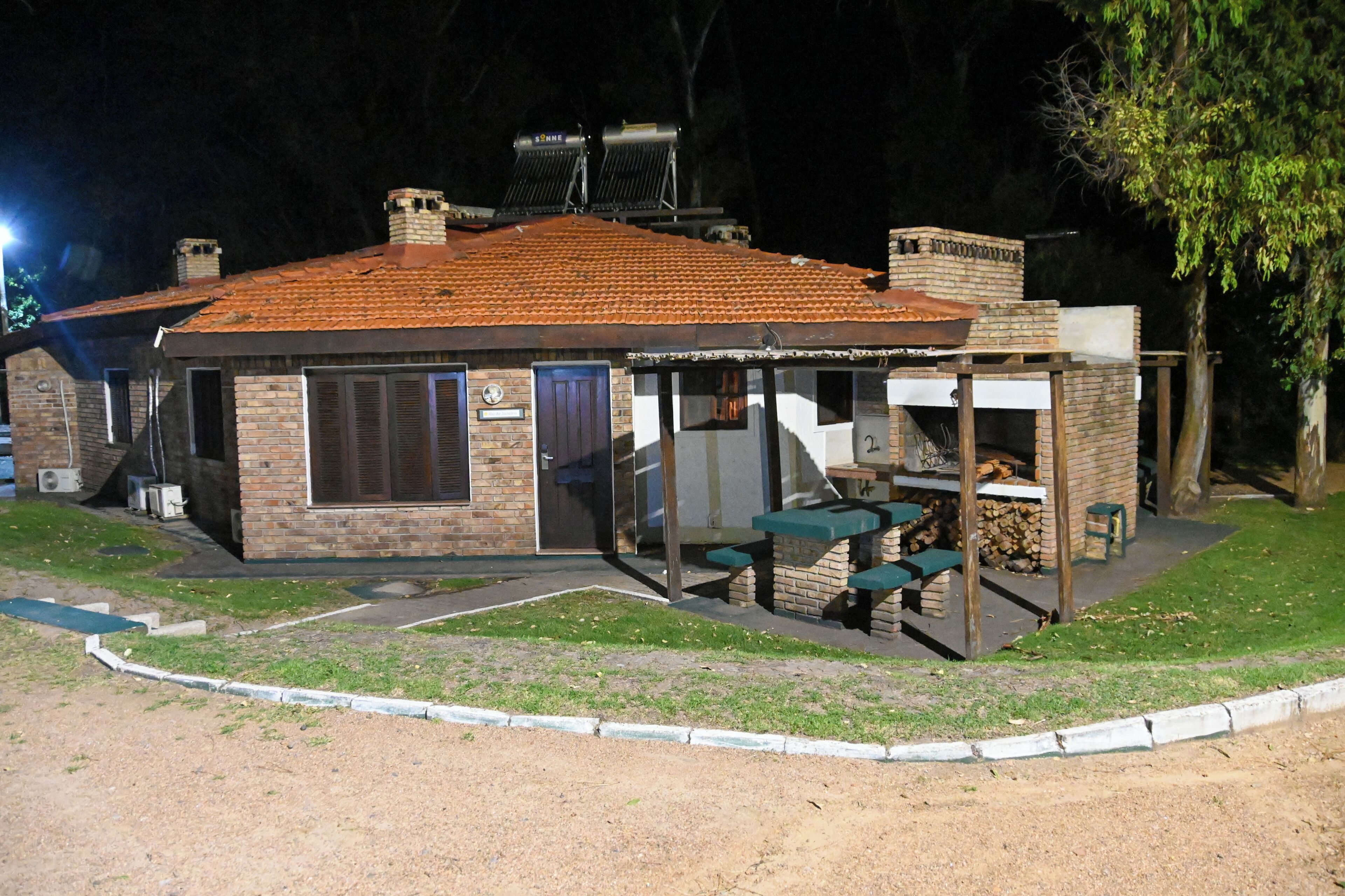 A small brick building with a tiled roof, a covered patio area with tables and chairs, and a chimney.