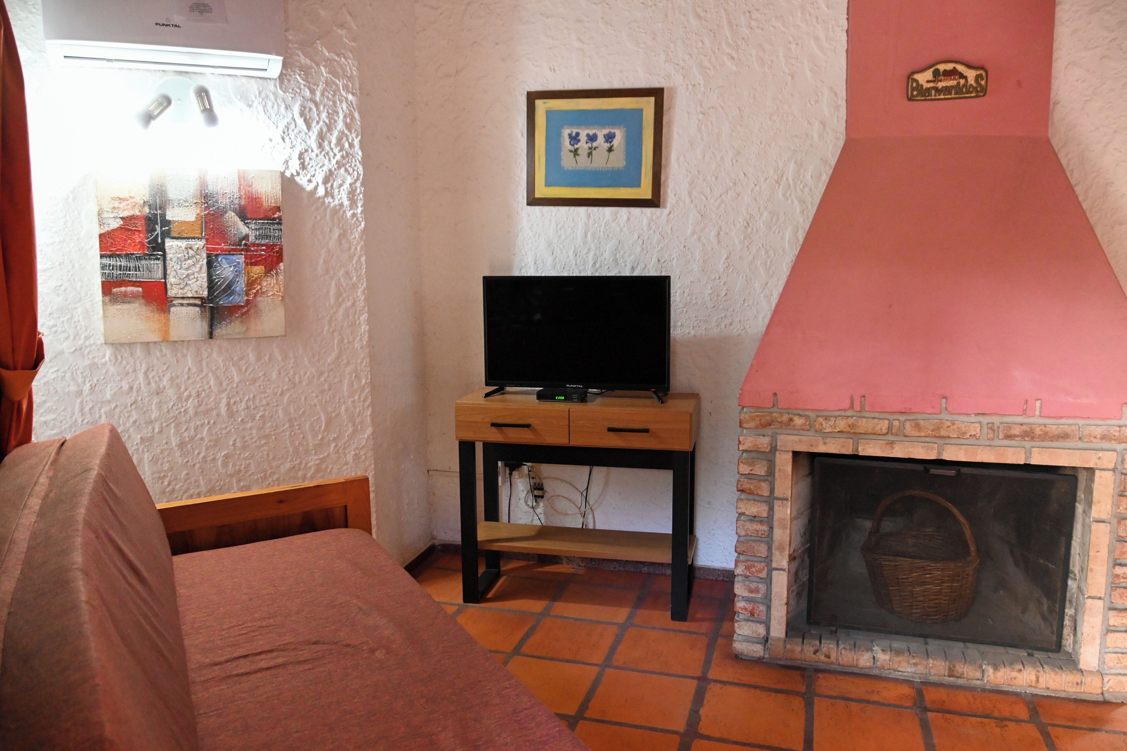 Una habitación con una cama, un televisor sobre un soporte de madera, una chimenea y un cuadro en la pared.