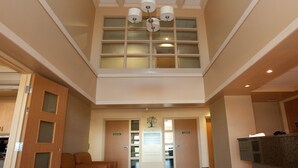 A hotel lobby with a high ceiling, a central chandelier, a reception desk, and a seating area.