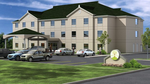 A multi-story hotel with a covered entrance, parking lot, and a sign with a tree and grass logo.