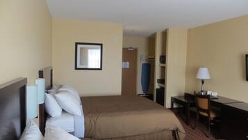 Une chambre d’hôtel avec deux lits, un bureau, une chaise, une lampe et un tableau encadré au mur.
