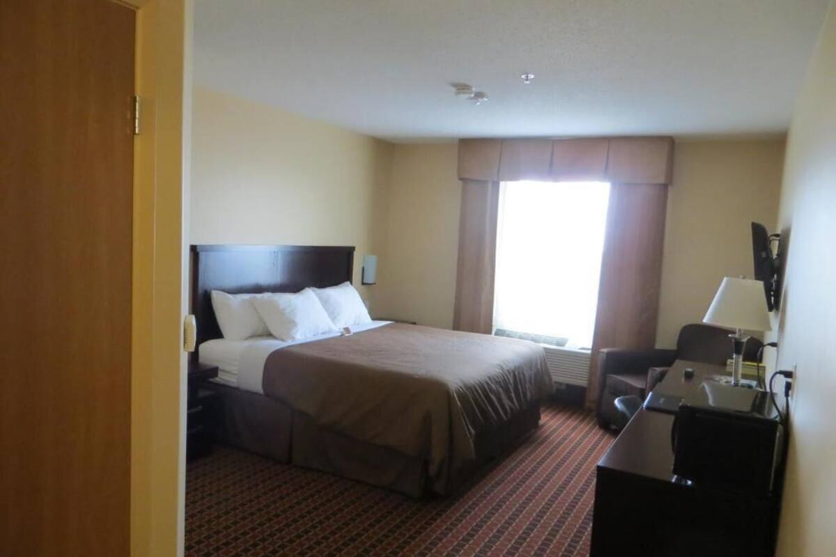 A hotel room with a bed, a desk, a chair, a lamp, and a window with curtains.