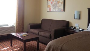 A hotel room with a bed, a sofa, a small table, a desk with a lamp, and a window with curtains.