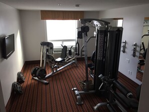 A hotel room with a gym area featuring exercise equipment, a television, and a window with a view.