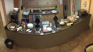 A breakfast bar with a variety of food items, utensils, and a coffee machine.