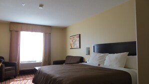 A hotel room with a large bed, a chair, a desk, and a window with curtains.