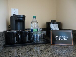 A coffee station with a coffee maker, mugs, a water bottle, and a sign reading "An Invitation To Fine Tea".